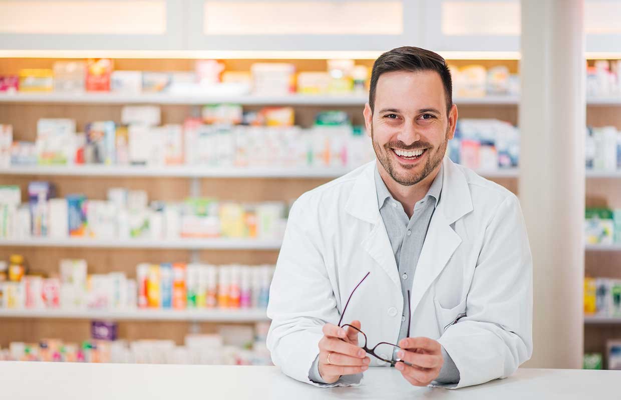 smiling young man in a white coat holding glasses in his hands