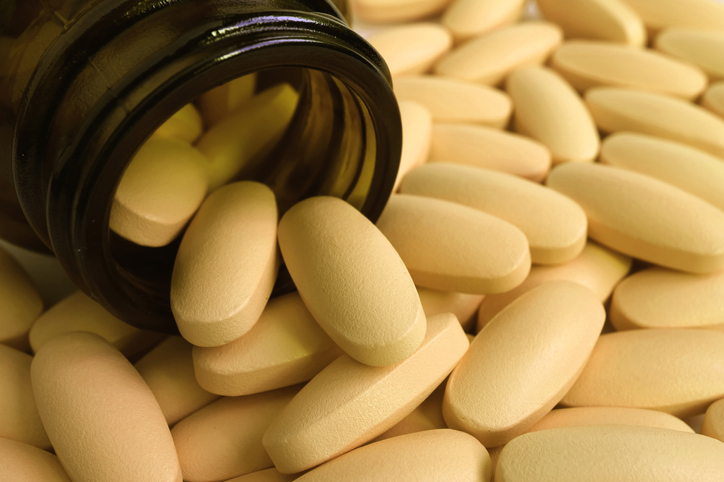 Pile of light yellow color oval shaped pills scattered from smoky glass bottle